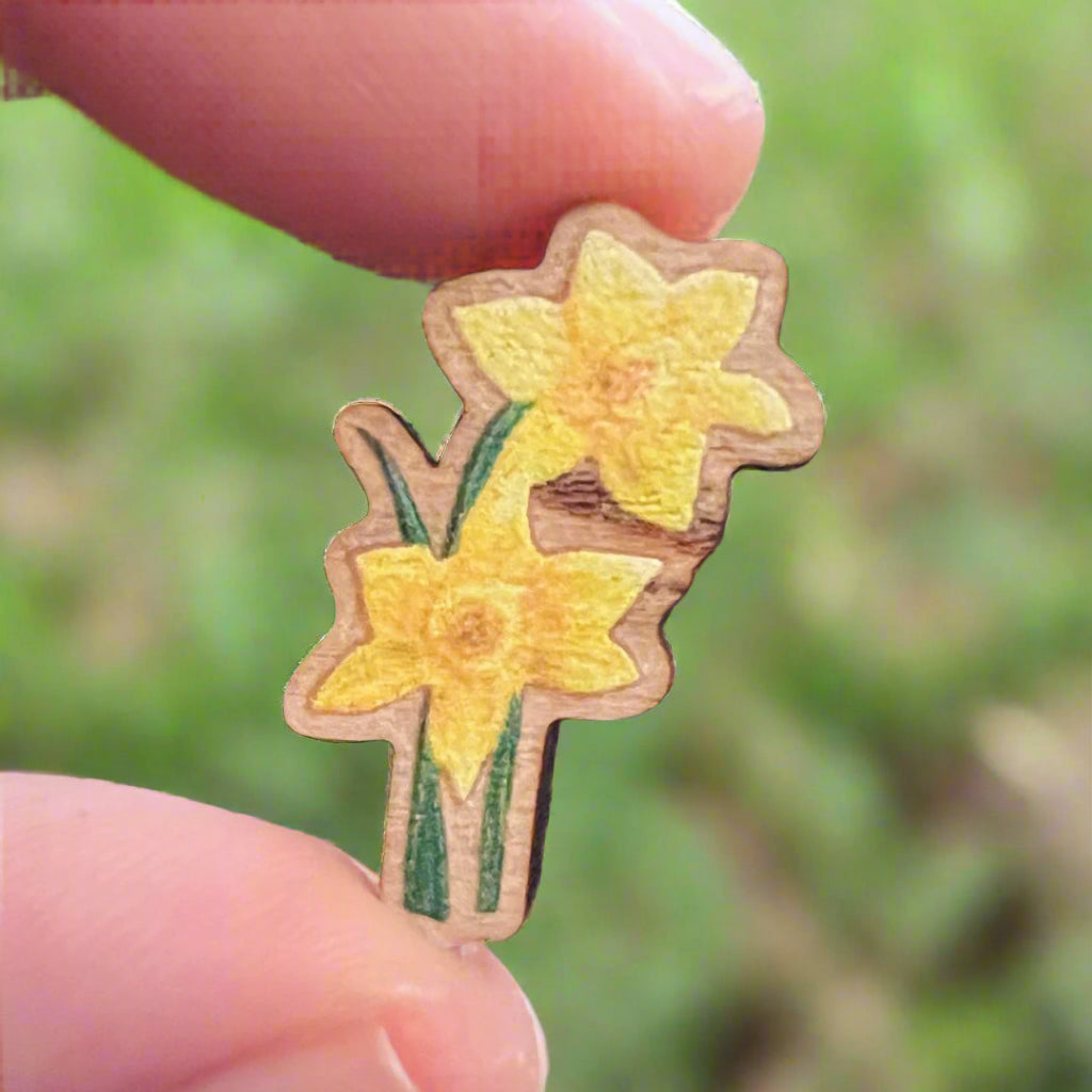 Daffodil printed die cut wooden pin held in front of blurred grass