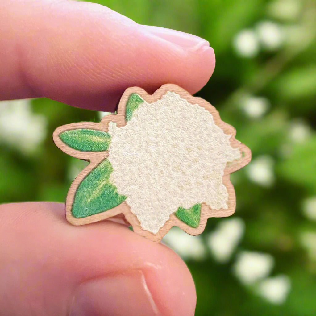 Elderflower die cut wooden pin held in in front of a blurry green garden