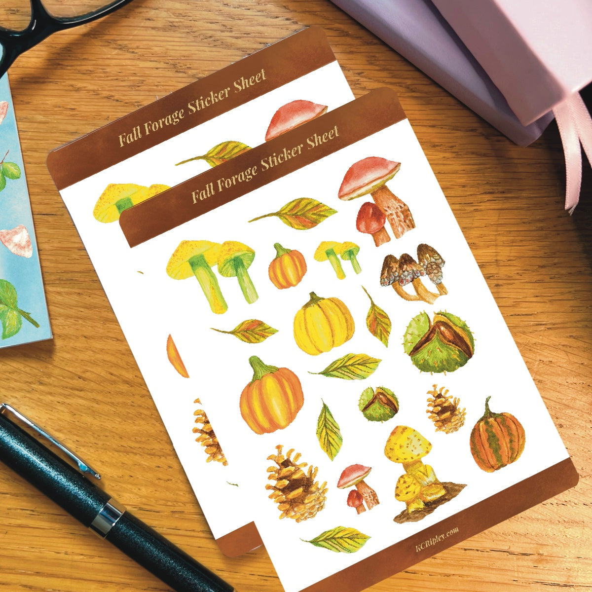 2 White sticker sheets with 20 colourful mushrooms and autumnal botanicals in a variety of sizes and colours, on a wooden desk with notepad, glasses and a pile of journals