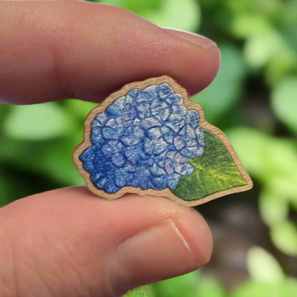 Blue hydrangea pin held in a garden with blurred background