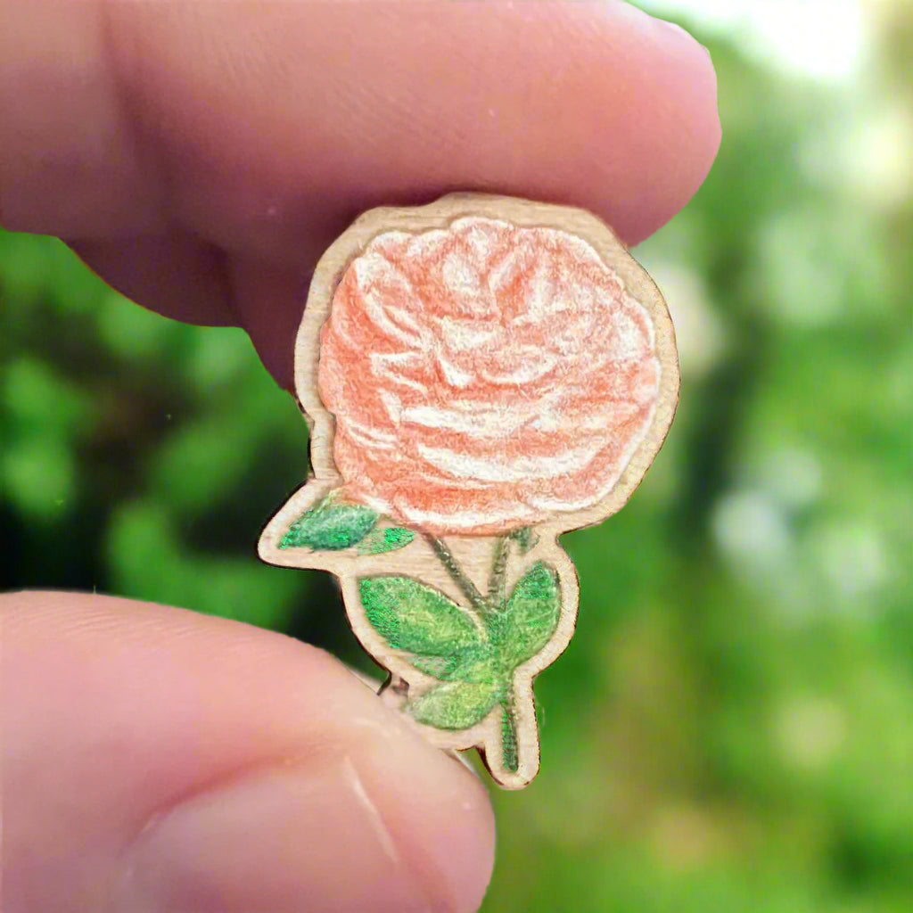 Peach rose die cut wooden pin held in front of bushes