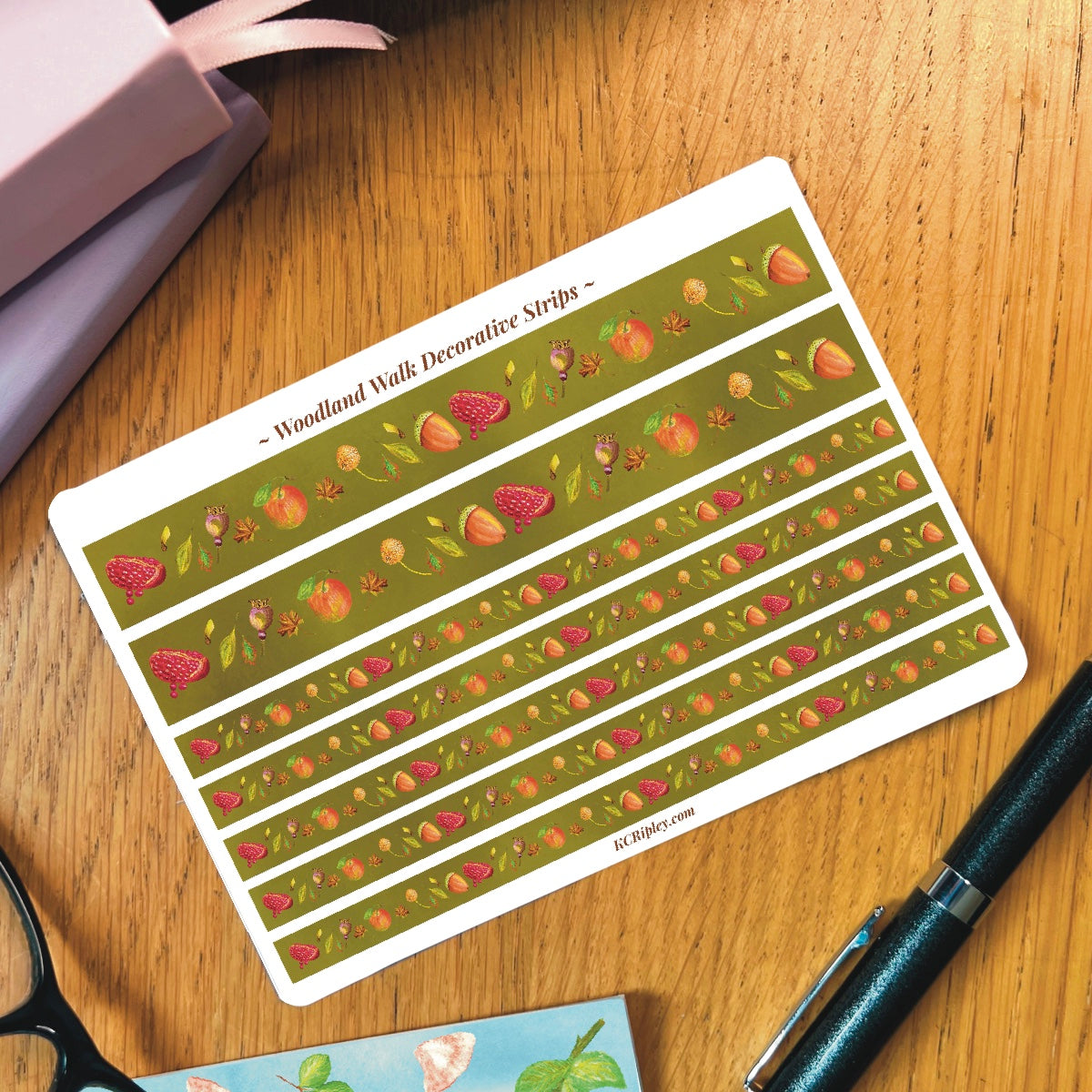 White sticker sheet with 2 wide and 5 narrow sticker strips in a moss green with a repeating botanical pattern featuring pomegranates, acorns, seeds and apples