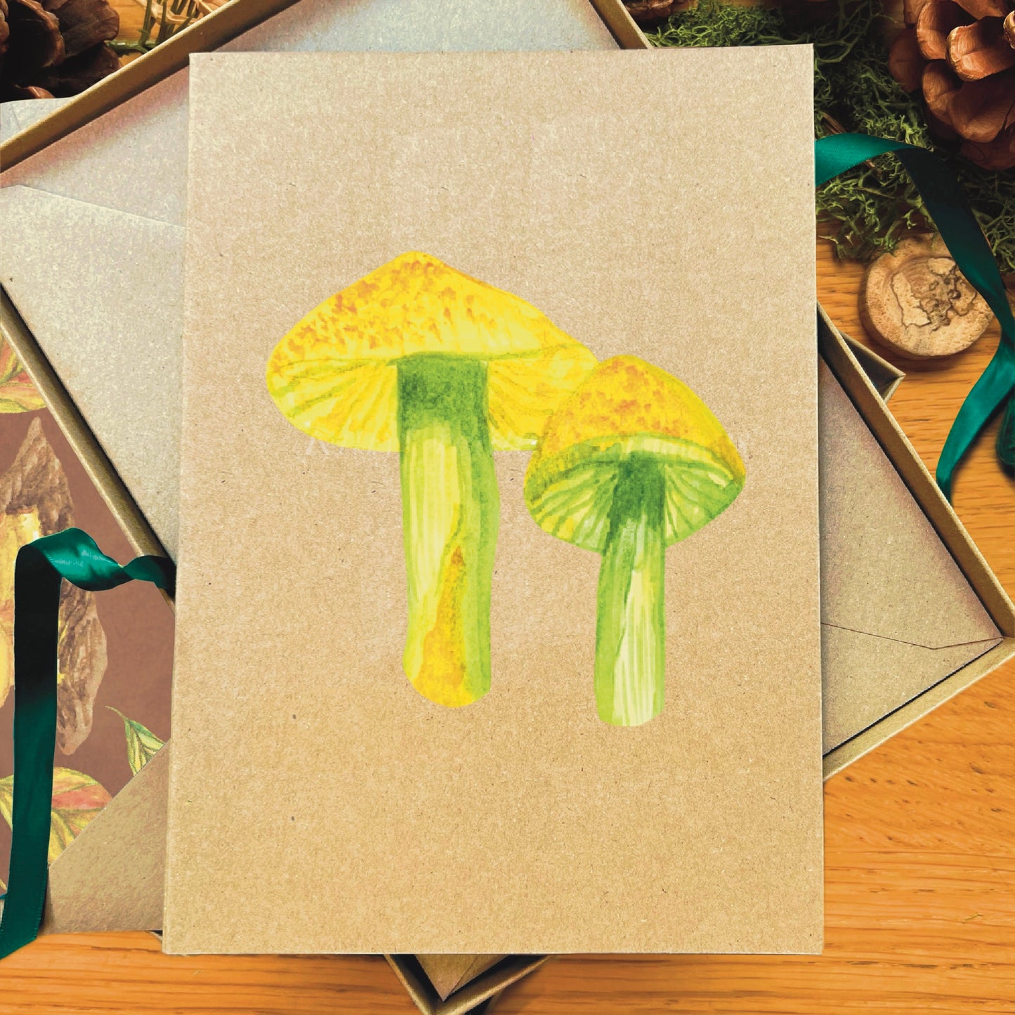 Green yellow parrot waxcap mushroom painted in watercolour attached to a natural recycled blank greetings card, laying in a box with an illustrated inlay envelope
