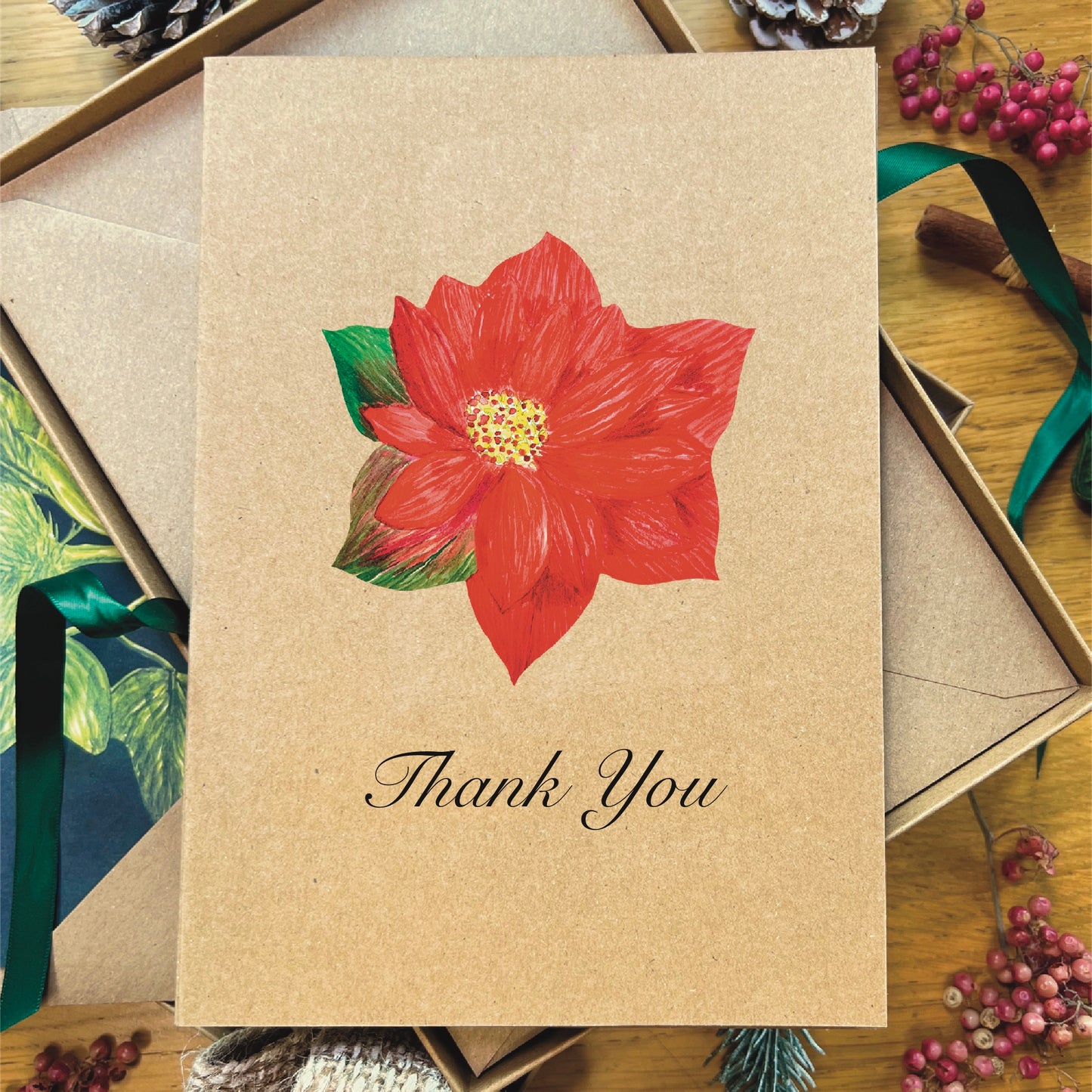 Red poinsettia painted in watercolour attached to a natural recycled blank greetings card, laying in a box with an illustrated inlay envelope