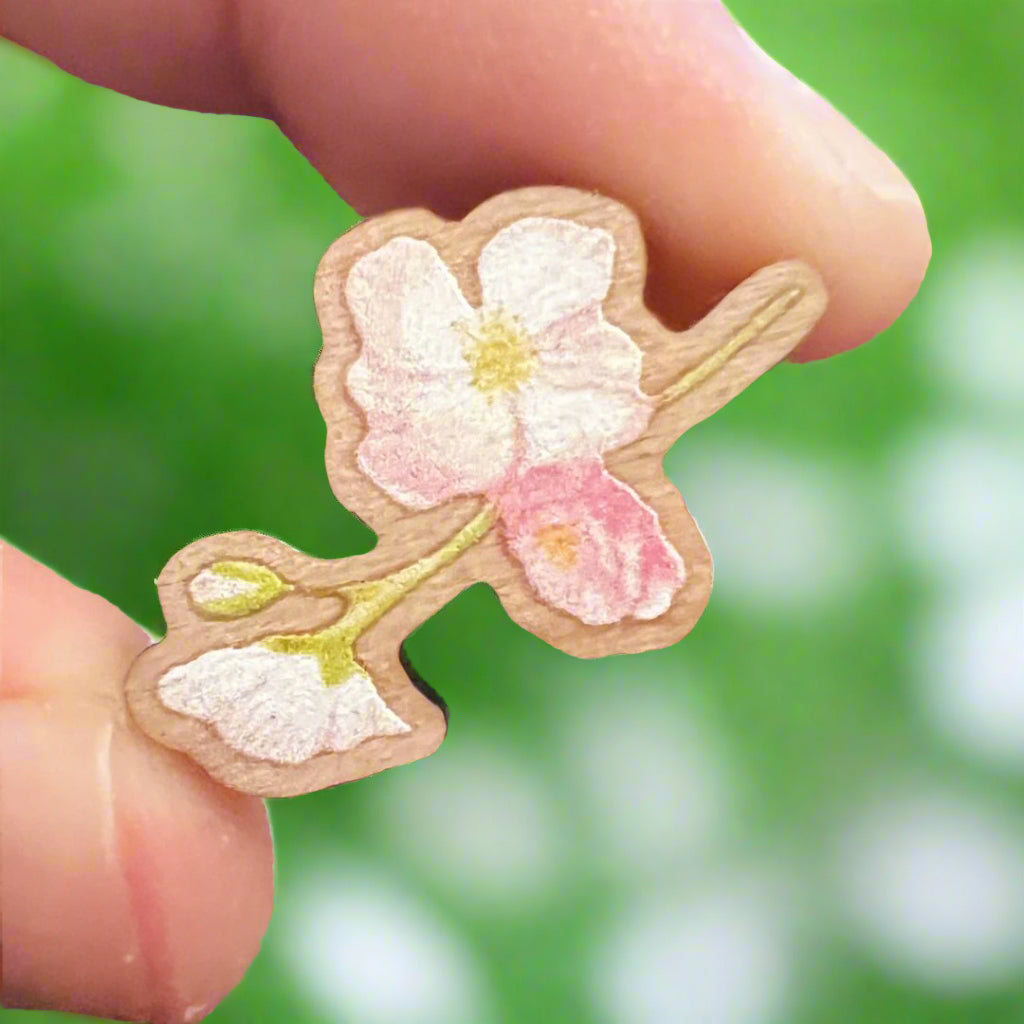 Cherry blossom wooden pin die cut and held in front of a blurry garden background