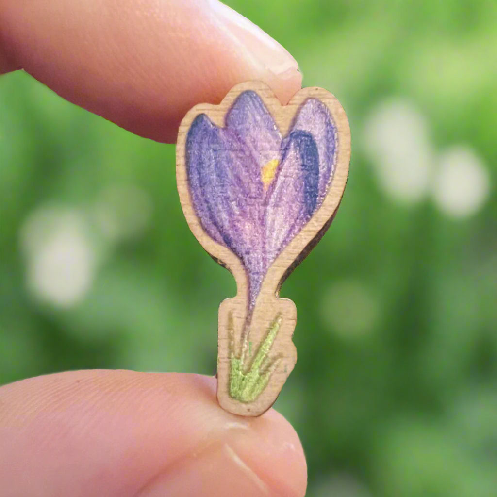 Crocus die cut wooden pin held in front of a blurry green and white garden background