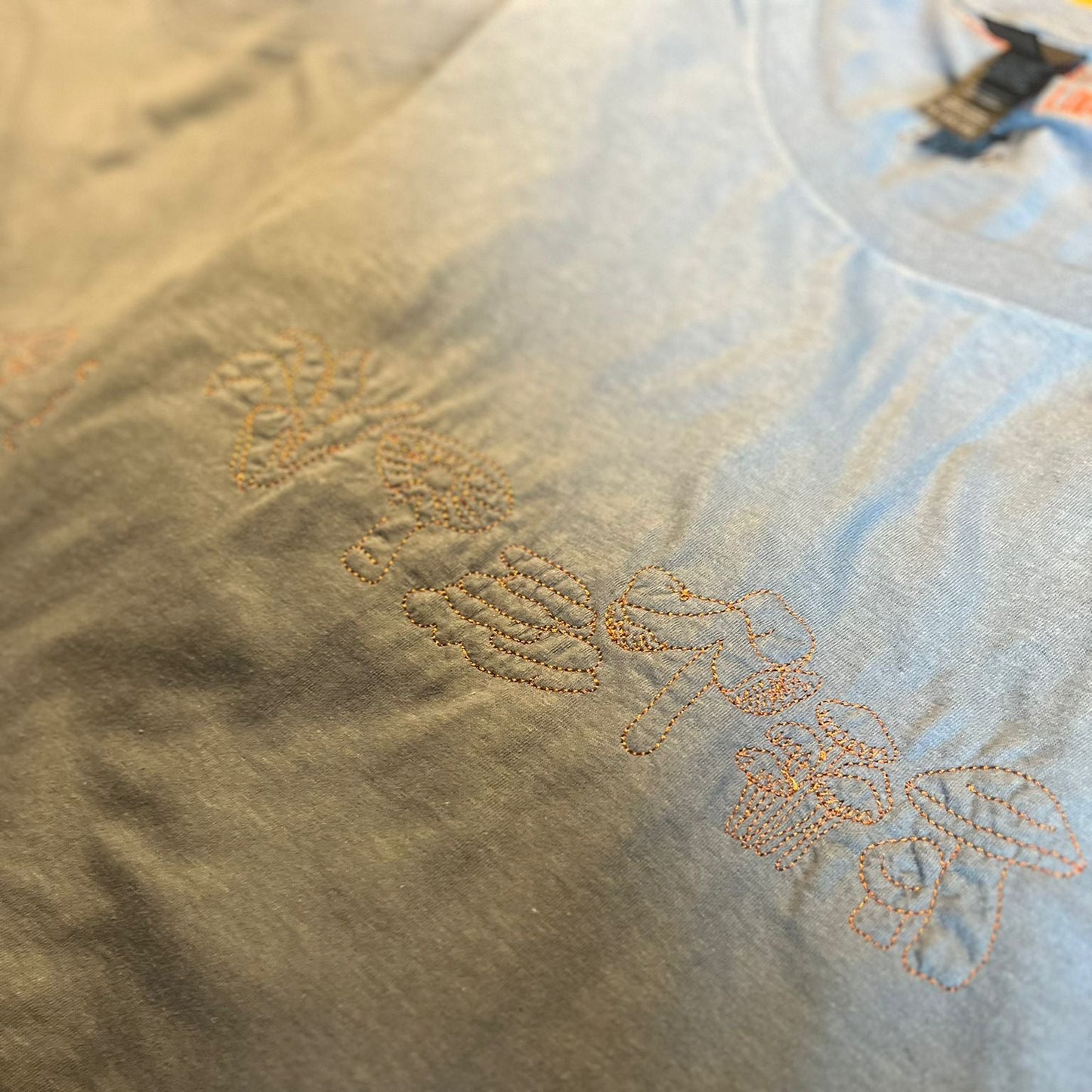 Green T-shirt with embroidered mushroom design on a wooden surface