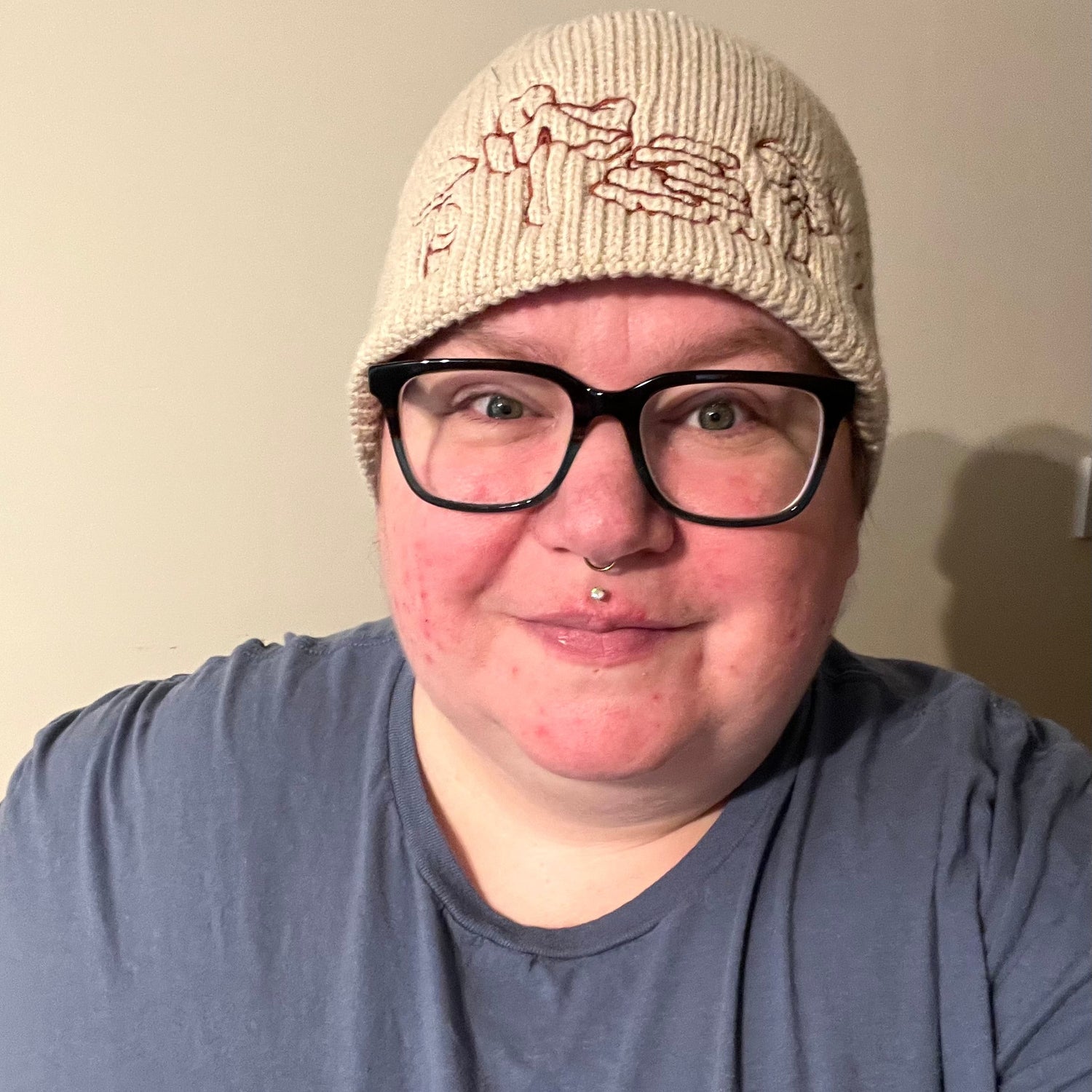 Person wearing a beige knit hat and black glasses with a plain background
