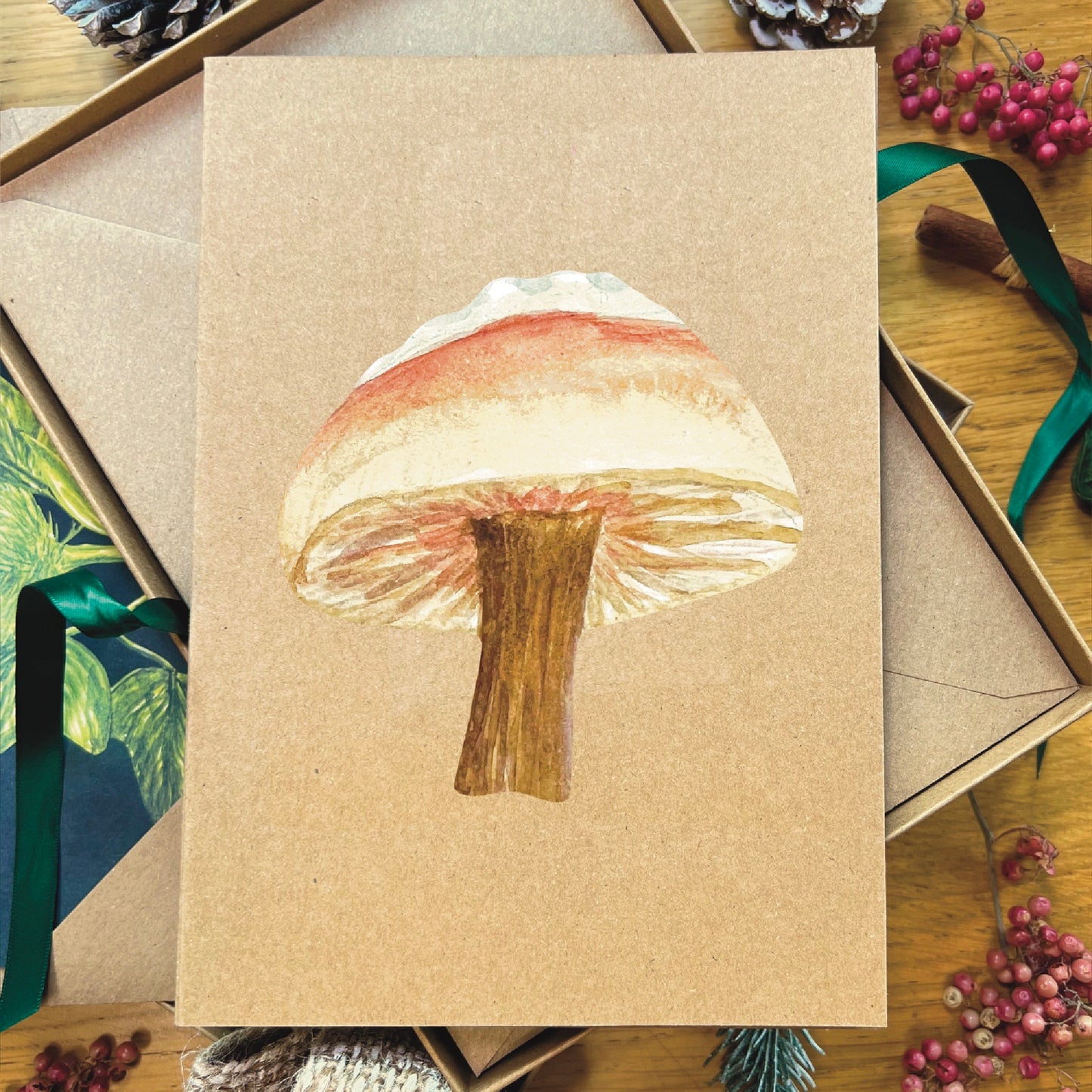 Snow topped slimy Waxcap mushroom illustrated in watercolour attached to Manila recycled greetings card on a wooden desk