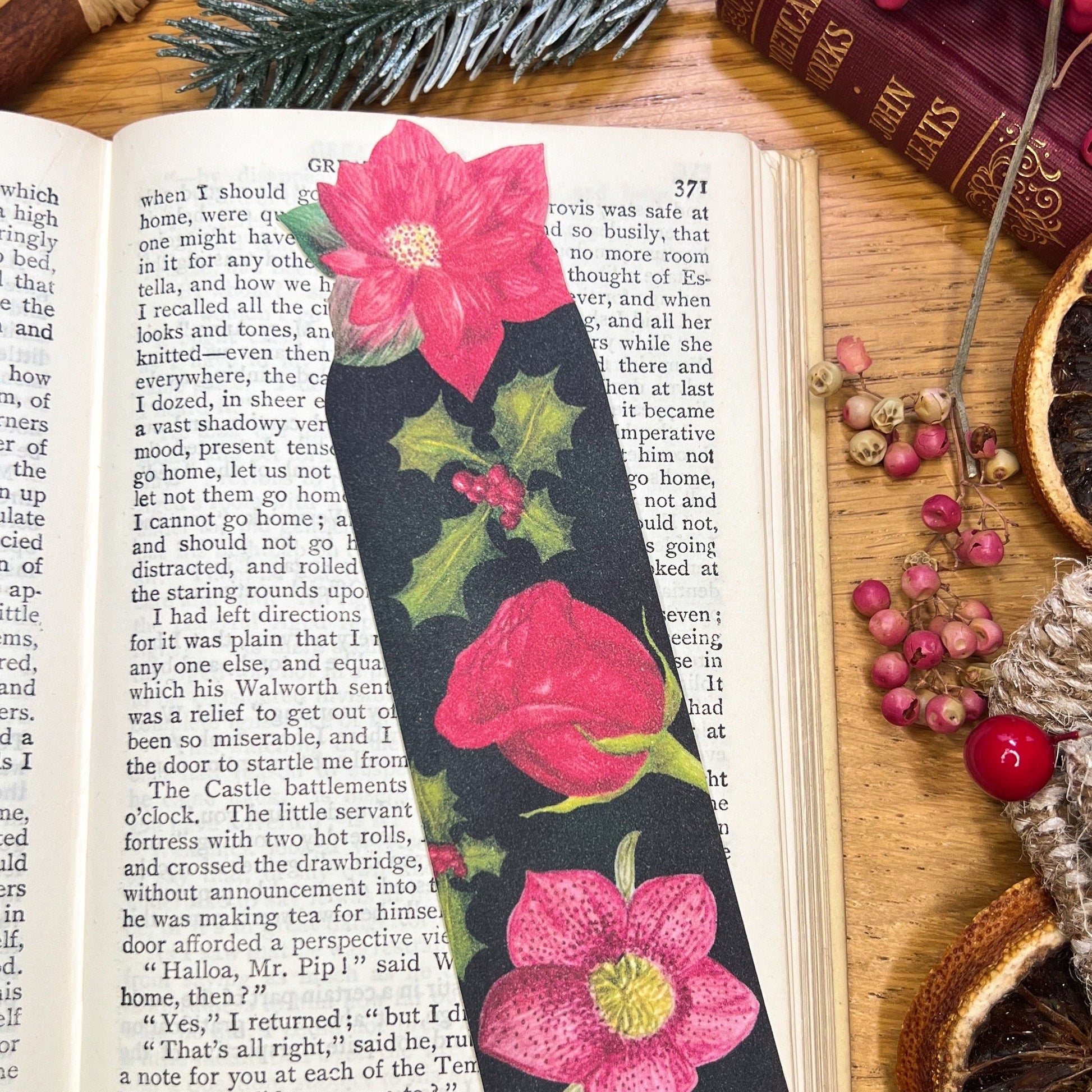 Winters bloom florals bookmark illustrated with hellebore, rose, holly and cut out at the top to the shape of a red poinsettia, resting on an open book